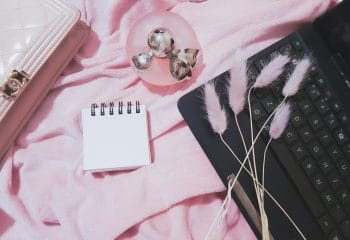 RIGA, LATVIA - FEBRUARY 27, 2021: Flat lay woman set: Chanel pink patent leather wallet, Nina Ricci fragrance perfume, notepad,   tablet PC, and fluffy spikelets of lagurus.